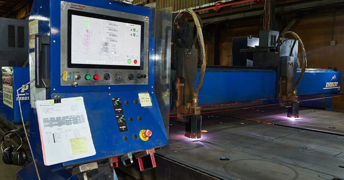 A close-up of a CNC plasma cutting machine featuring a blue control panel with buttons, a screen, and documents attached for reference.